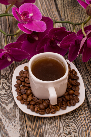 Small white cup of coffee, roasted coffee beans, orchid on wooden backgroundの写真素材