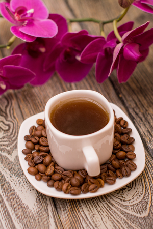 Small white cup of coffee, roasted coffee beans, orchid on wooden backgroundの写真素材