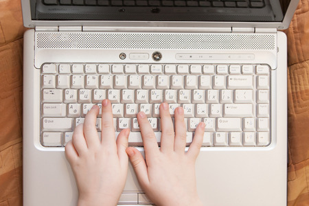 Photo Kid's Hands typing keyboard on desk wood.
