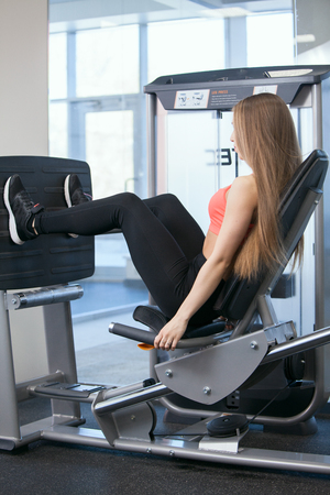 Beautiful young girl engaged in fitness in the gym. Brunette performs exercises on the simulator.