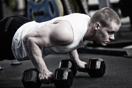 Man doing push up holding dumbbell at the gymの写真素材
