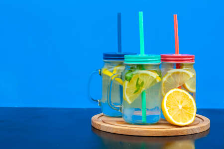Glass with lemonade or mojito cocktail with lemon and mint, cold refreshing drink or beverage with ice on blue background.の写真素材