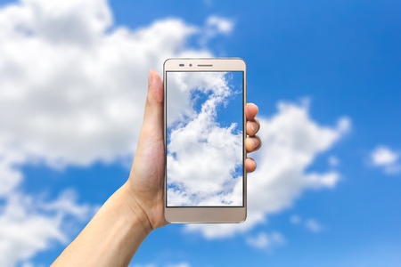 hand holding smartphone on blue sky backgroundの写真素材