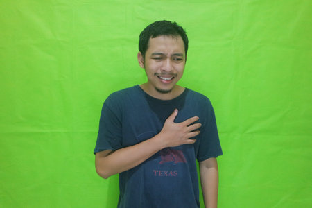 Asian man holding his chest in pain isolated on green backgroundの写真素材