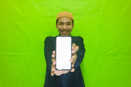 Asian muslim young man showing smartphone with blank screen isolated on green backgroundの写真素材