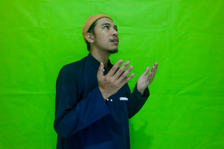 Religious asian muslim man praying isolated on green backgroundの写真素材