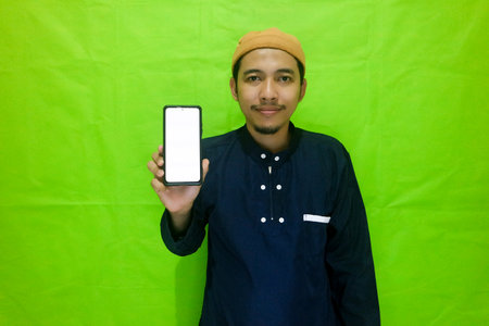 Asian muslim young man showing smartphone with blank screen isolated on green backgroundの写真素材
