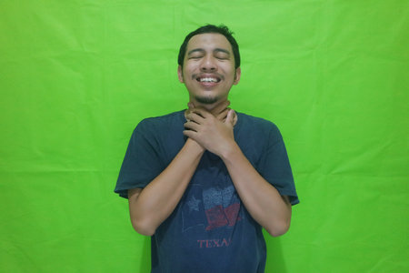 Sick asian man with sore throat isolated on green backgroundの写真素材