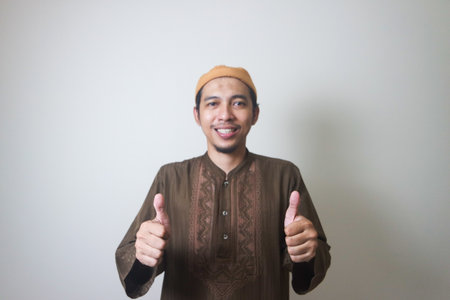 Portrait of attractive Asian muslim man in white shirt showing thumb up, good job hand gesture....