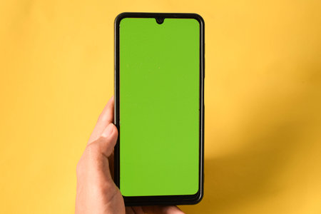 hand holding modern mobile phone green screen isolated on yellow backgroundの写真素材