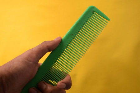 hand hold green comb on yellow backgroundの写真素材