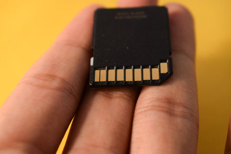 Close up hand holds SD Card for DSLR or Mirrorless camera on yellow background