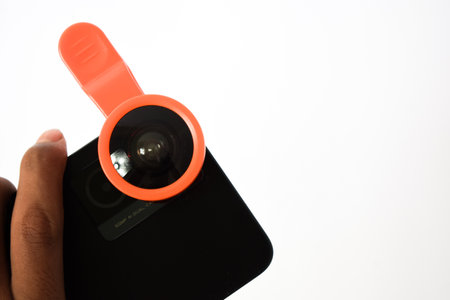 Hand holding extension fisheye lens on black smartphone isolated white background