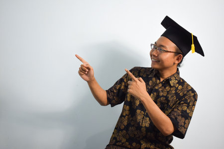 Expressive of Adult indonesia male wear batik, toga cup or graduation hat and eyeglasses isolated on white background, expressions of portrait graduationの写真素材