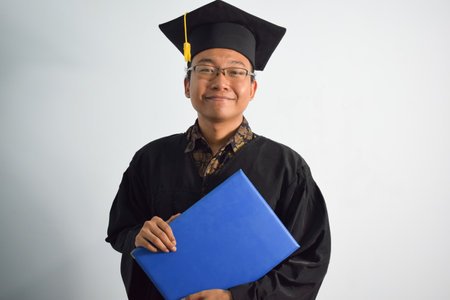 Expressive of Adult indonesia male wear graduation robe, hat and eyeglasses, Asian Male graduation bring blank blue certificate isolated on white background, expressions of portrait graduationの写真素材