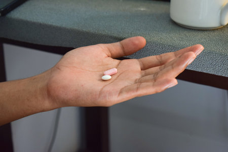 A man taking pills from bottle infront of table workspace, healthcare concept