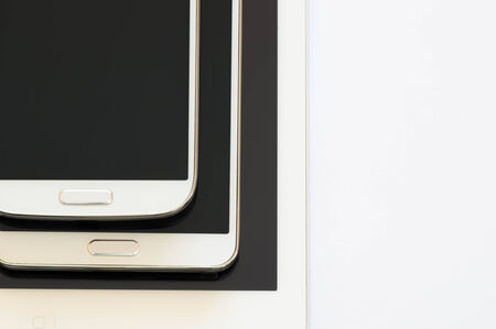 Upper shot of a white tablet on which is located a phablet which hold a smartphone