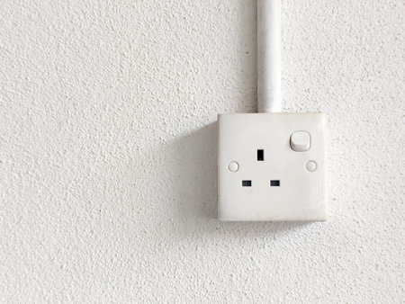 British style three pin electrical socket with switch mounted on a textured white wall and conduit...