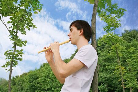 young man playing on flute at summer time outdoor side view