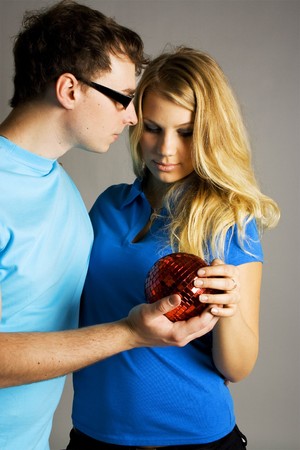 young man in glasses and beauty blond girl holding red ball for christmas treeの写真素材