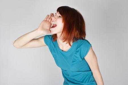 young redhead woman calling someone, hand near lips, side view, half bodyの写真素材