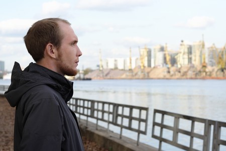 portrait of young man standing on river embankment and looking into the distanceの写真素材