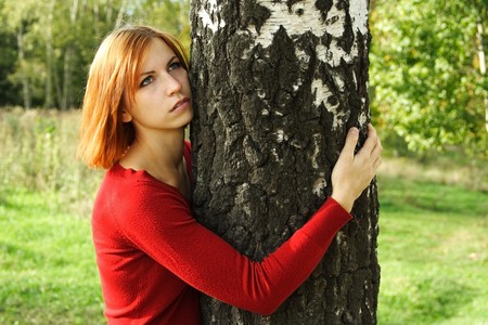 beauty girl in red dress hug a tree, half body, looking at sideの写真素材