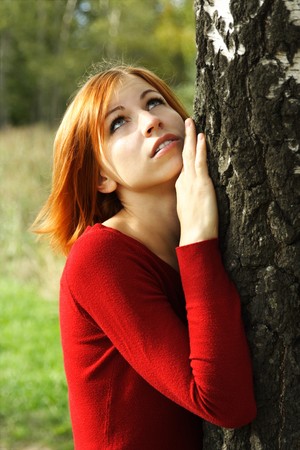 beauty girl in red dress snuggle up to tree, half body, looking upの写真素材
