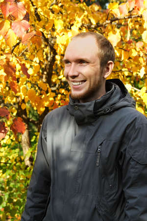 young man with beard outdoor, smiling and looking at side, autumn tree on background の写真素材