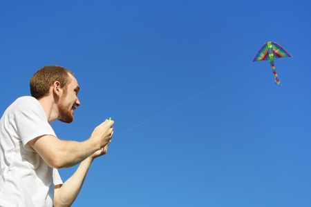 young man in white shirt flying kite, half body, blue skyの写真素材