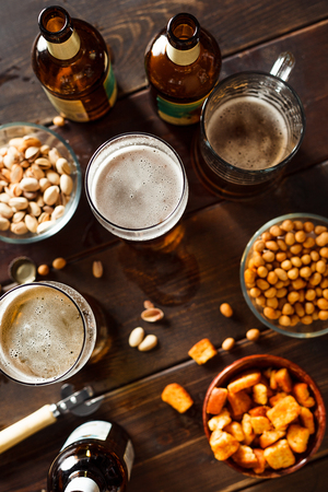 Overhead view of beer glasses, beer dottkes and snacks on wooden table. Focus on beerの写真素材