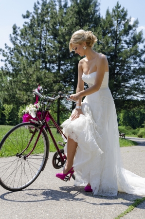 Charming image of a bride with a bicycle wearing purple shoes. The shot was made on a sunny day in the park.の写真素材