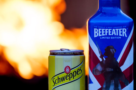 Schweppes can and  Beefeater gin bottle with fire in the background.のeditorial素材