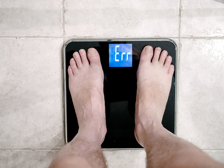 Closeup of man's feet on weight scale indicating errorの写真素材