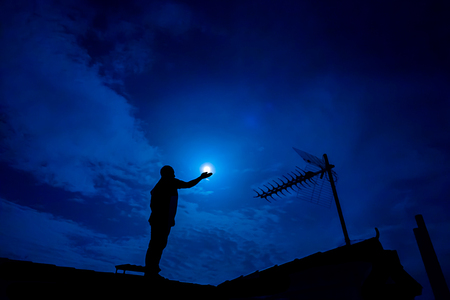 Man up on the roof,  holding full moon in hand against night skyの写真素材