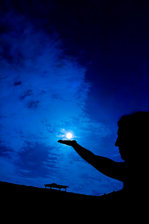 Woman holding full moon in hand against night skyの写真素材