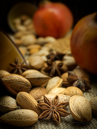 Autumn composition of pomegranates on a dark rustic background with almonds, apricot jam and star aniseの写真素材