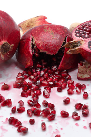 Ripe pomegranate with cracks and splashes of juice and seeds on white backgroundの写真素材
