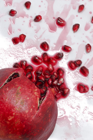 Ripe pomegranate with cracks and splashes of juice and seeds on white backgroundの写真素材