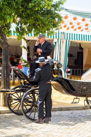Seville, Spain - April 23, 2015: Carriage drivers dressed in tradional "traje corto" with casetas behind. The Seville Fair "Feria de abril de Sevilla" is one of most important celebration of the city, it begins one or two week after easter Holy Weekのeditorial素材