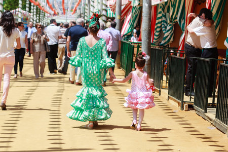 Seville, Spain - April 28, 2015: Mother and daughter in traditional dress walking alongside Casetas at the Seville Fair. The Seville Fair "Feria de abril de Sevilla" is one of most important celebration of the city, it begins one or two week after easter のeditorial素材