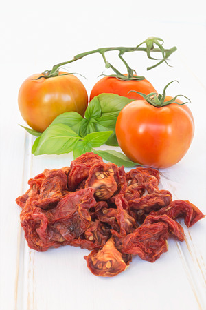 Fresh leaves of basil with dry tomatoes on wooden tableの写真素材