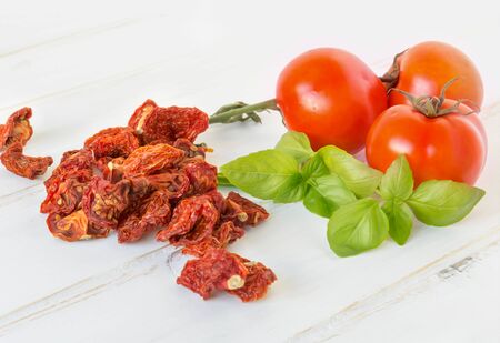 Fresh and dried tomatoes and basil on wooden tableの写真素材