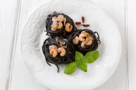 Plate of black spaghetti with prawn on white tableの写真素材