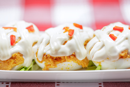 Close up of Stuffed eggs with tuna, tomato, mayonnaise and red pepper on red tableclothの写真素材