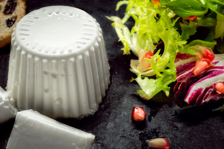 Close up of Fresh cheese with salad of fresh vegetables and pomegranate on dark slate stoneの写真素材