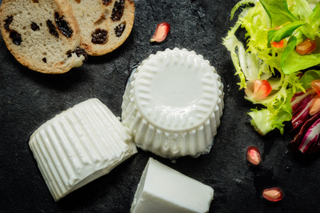 Close up of Fresh cheese with salad of fresh vegetables and pomegranate on dark slate stoneの写真素材