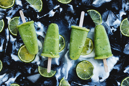 Healthy lime yogurt popsicles on ice cubes over black background. Refreshing summer dessertの写真素材
