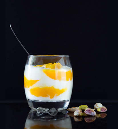 Healthy breakfast. Greek yogurt and Mango pieces in glass with pistachios on black board. Detox food concept.の写真素材