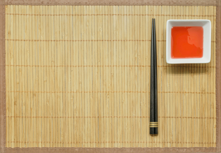 Black Wooden chopsticks and sweet and sour sauce on bamboo mat background.の写真素材